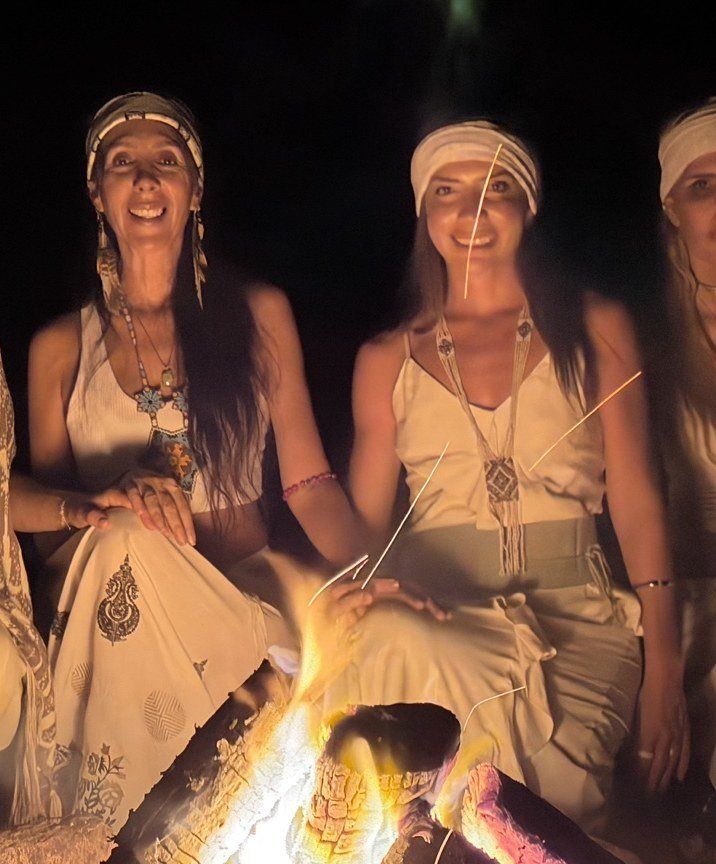 Mulheres vestidas de branco sentadas ao redor de uma fogueira, à noite