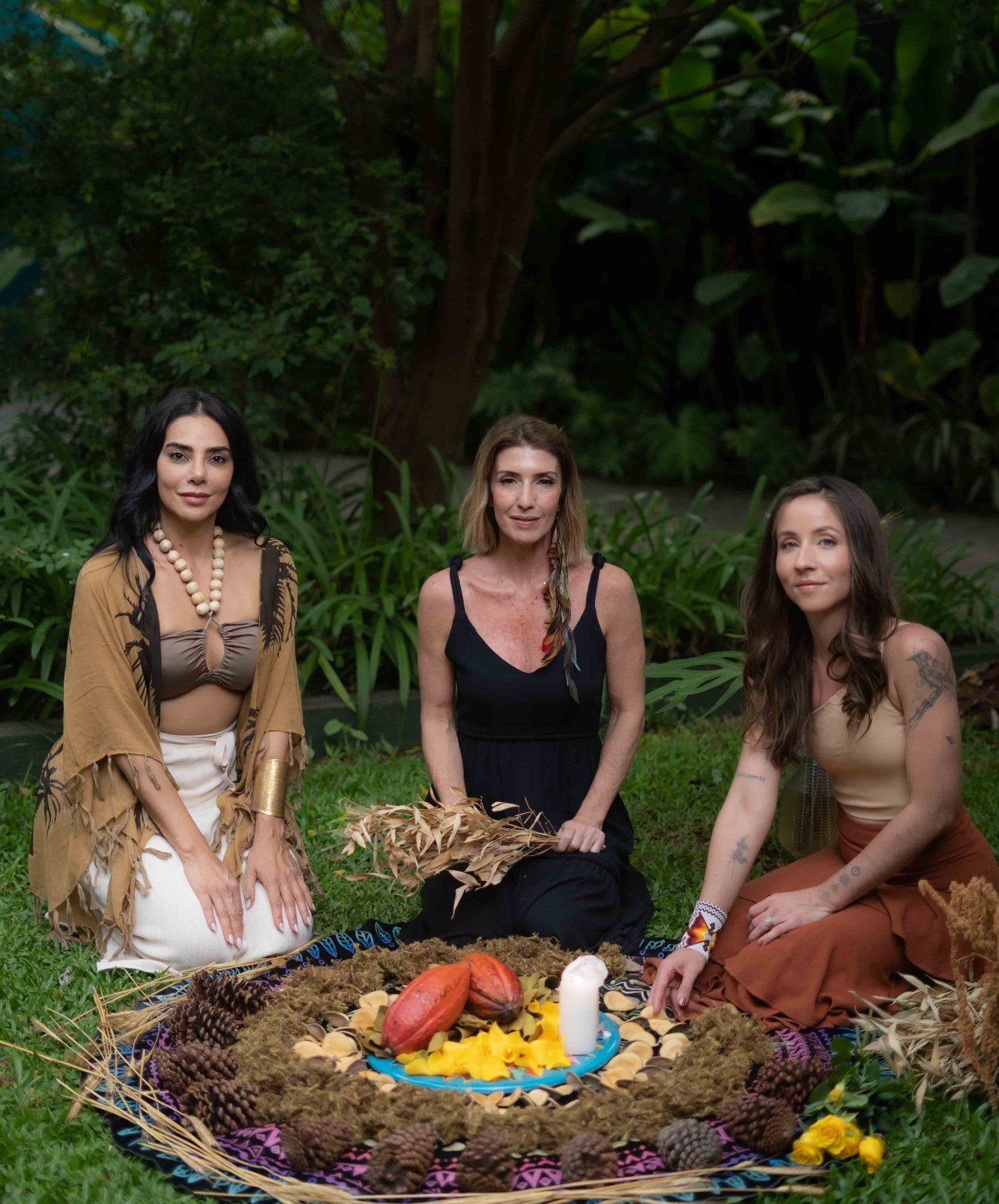 Elini e duas facilitadoras sentadas ao redor de um altar de cacau, no jardim